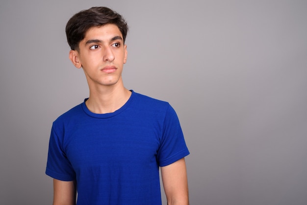 Studio shot of young handsome Persian teenage boy against gray background