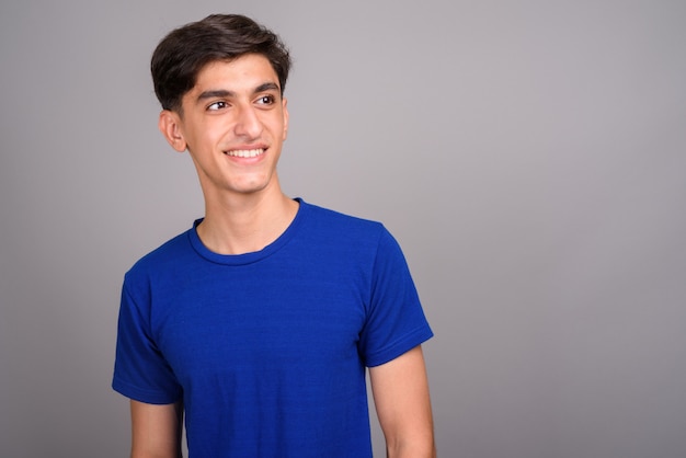 Studio shot of young handsome Persian teenage boy against gray background