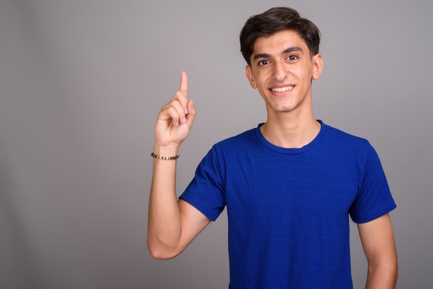 Studio shot of young handsome Persian teenage boy against gray background