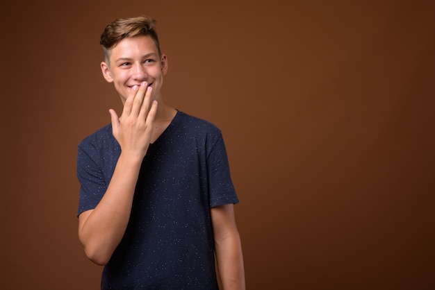 Studio shot of young handsome teenage boy against brown backgrou