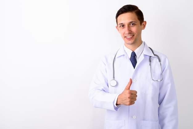 Studio shot of young happy man doctor smiling while giving thumb