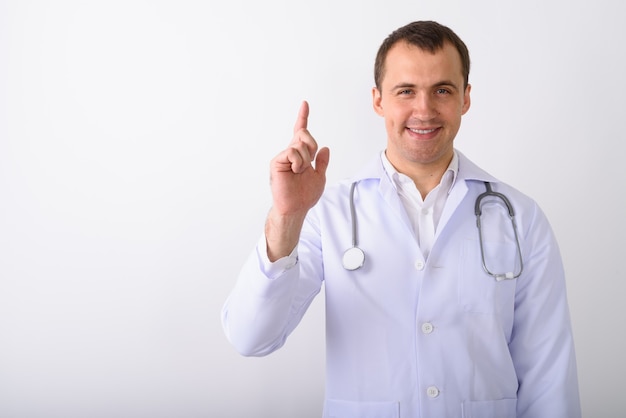 Studio shot of young happy muscular man doctor smiling while poi