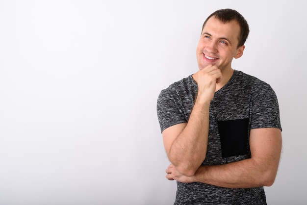 Studio shot of young happy muscular man smiling while thinking a