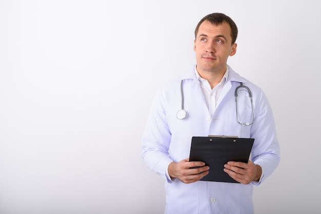 Studio shot of young muscular man doctor thinking while holding