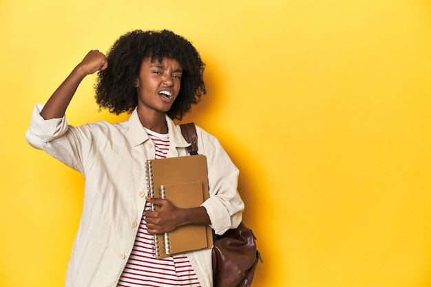 Studious teen girl with backpack and notebooks raising fist after a victory winner concept