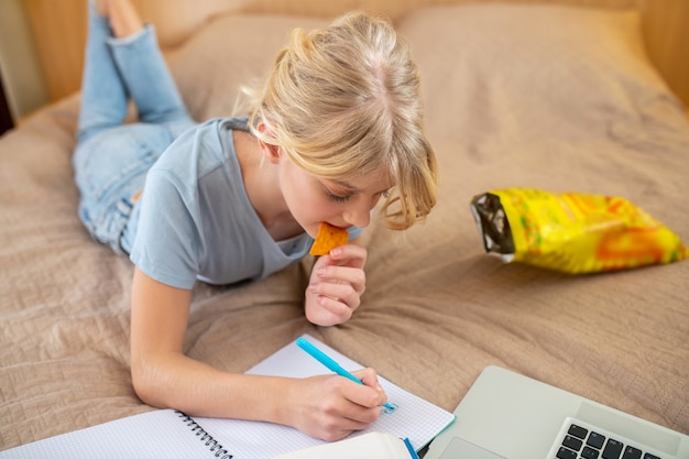 Studying from home. A teen girl lying on the bed and doing her lessons