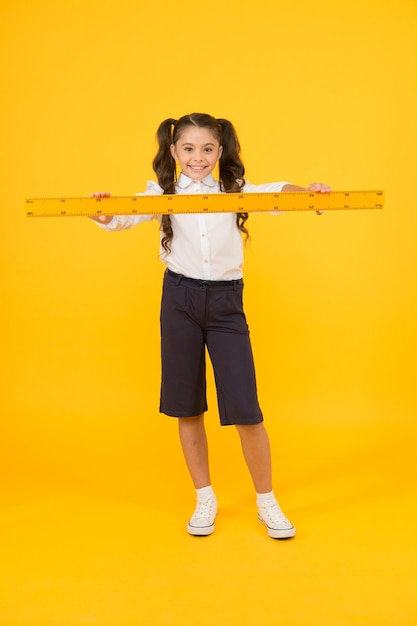 Studying is fun School adorable student study geometry Kid school uniform hold ruler Pupil cute girl with big ruler Geometry school subject Education and school concept Sizing and measuring