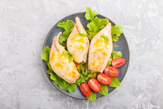 Stuffed baked squid with greens on a blue ceramic plate on a gray concrete background 