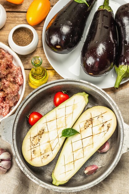 Stuffed eggplant ready to bake with ground meat, vegetables, and spices. Wooden background, kitchen utensil, rustic style, top view