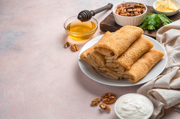 Stuffed homemade pancakes on a light background with sour cream, honey and nuts. Top view, copy space. Mardi Gras.