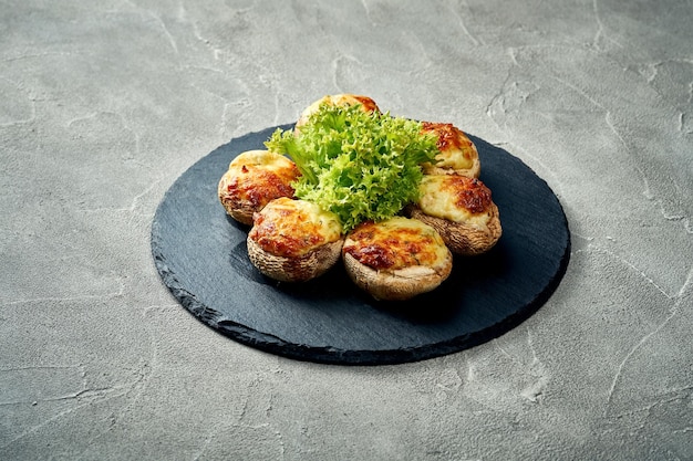 Stuffed mushrooms with meat and melted cheese on a black board