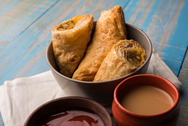 Stuffed vegetable puff or samosa, famous Indian Bakery snack, served with Tomato Ketchup and hot tea, selective focus