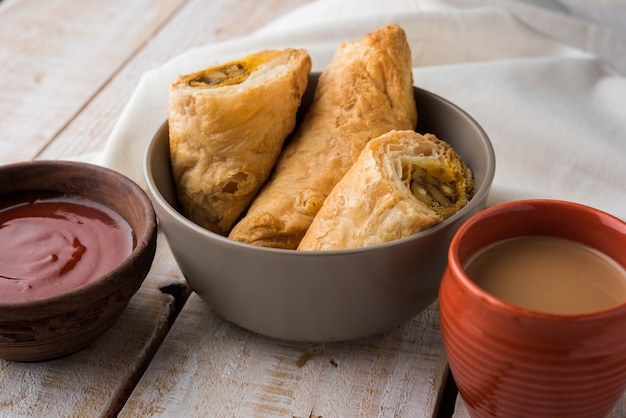 Stuffed vegetable puff or samosa, famous Indian Bakery snack, served with Tomato Ketchup and hot tea, selective focus