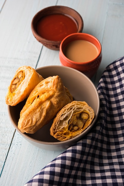 Stuffed vegetable puff or samosa, famous Indian Bakery snack, served with Tomato Ketchup and hot tea, selective focus