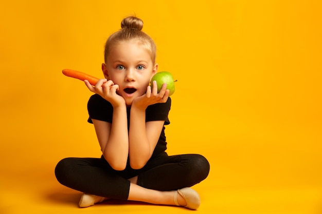 Stunned little girl in swimsuit and dance shoes choosing healthy food and looking at camera sitting