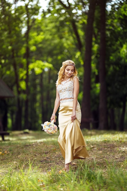 Stunning blonde bride stands among green bushes in the garden