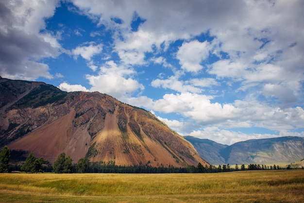 Stunning mountain landscape on sunny summer day. Spacious plain, pasture, high cliffs, blue sky with white clouds.