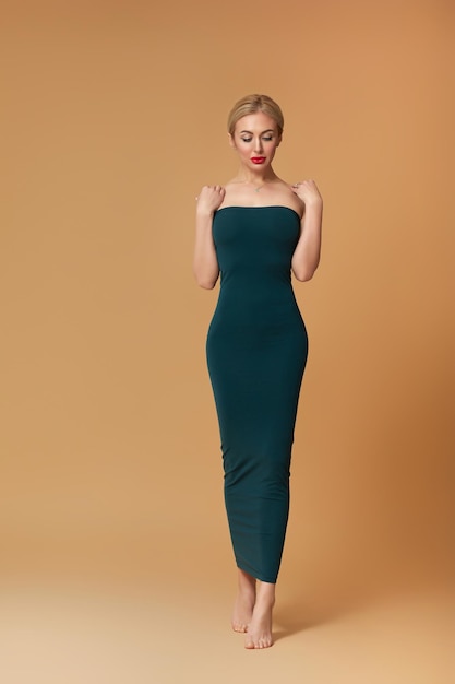 Photo stunning slim blonde woman in dark green dress on beige background