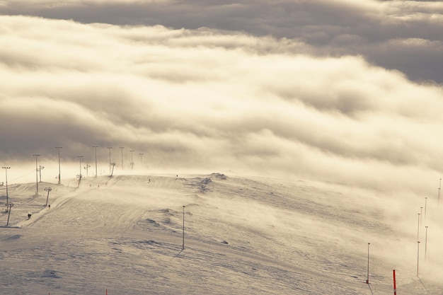 Stunning views of the ski slope and ski lift on the mountain in the middle of the clouds below and in front, sunset.