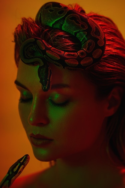 Stunning woman in a mix of red and green light with a python snake gracefully positioned on her head like a crown