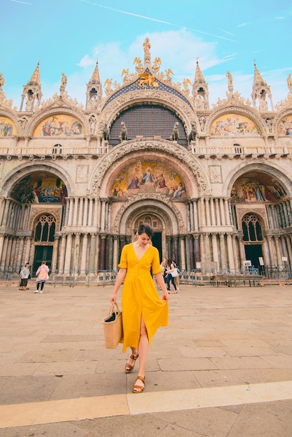 Stunning woman in yellow dress walking by city square basilica saint marco on background