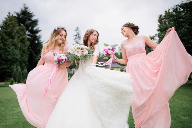 Stunning young bride and bridesmaids in pink dresses with wedding bouquets in the park