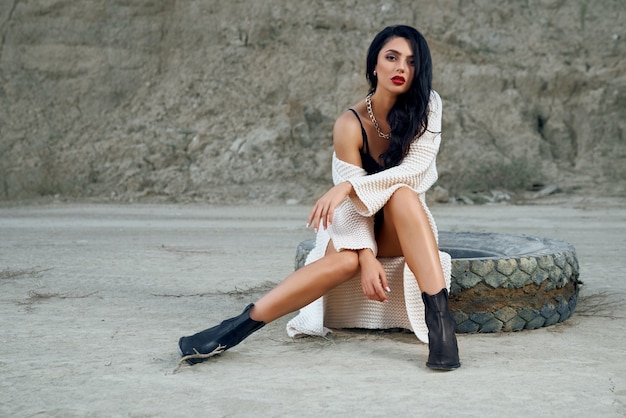 Stunning young lady with long dark hair dressed in trendy bodywear posing among empty sand quarry.