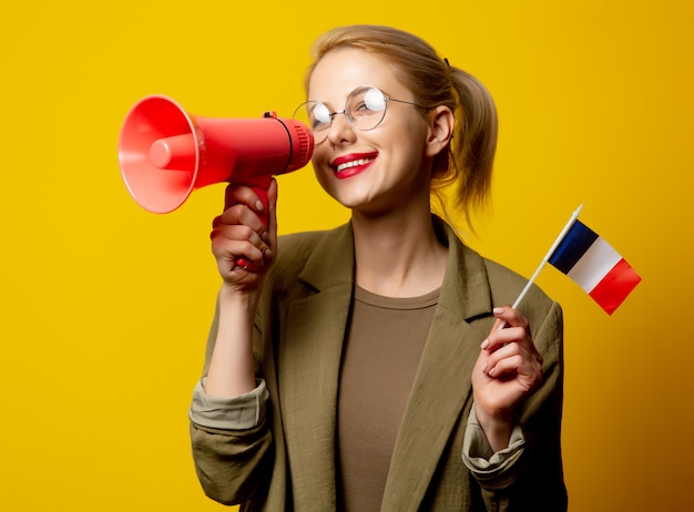 Style blonde woman in jacket with French flag and megaphone on yellow