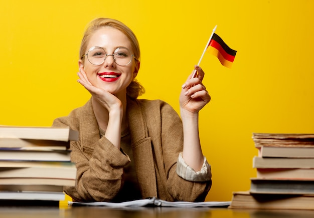 Style blonde woman sitting at table with books and flag of Germany on yellow