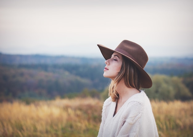 Style girl in sweater and hat at countryside with mountains on background