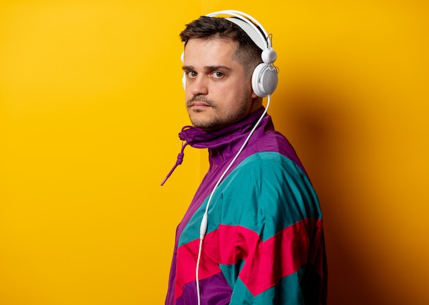 Style man in 90s tracksuit with headphones on yellow wall