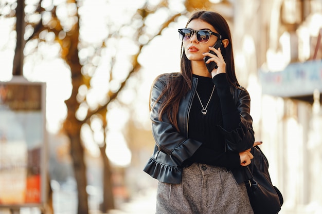 styligh woman uses her cell phone as she walks through the city on a sunny warm day