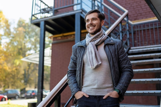 Stylish adult man with a wide smile stands and looks at the street