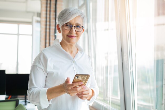 stylish adult woman in office with mobile phone near window