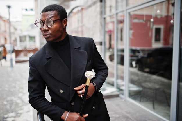 Stylish african american gentleman in elegant black jacket holding retro walking stick as cane flask or tippling cane with golden diamond ball handle Rich fashionable afro man