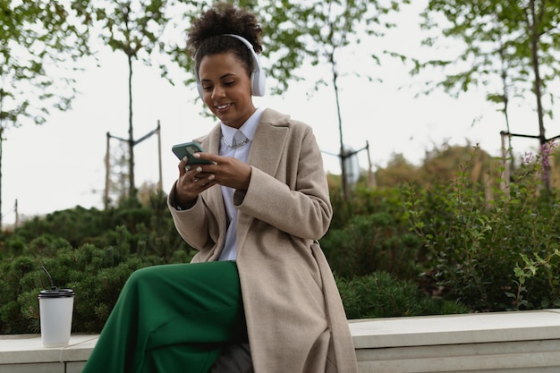 Stylish african american girl in headphones listening to music while looking at the phone