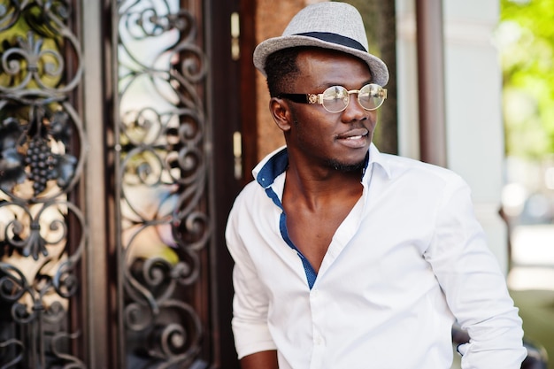 Stylish african american man in white shirt and colored pants with hat and glasses posed outdoor Black fashionable model boy