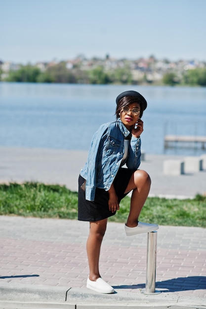 Stylish african american model in glasses hat jeans jacket and black skirt posed outdoor