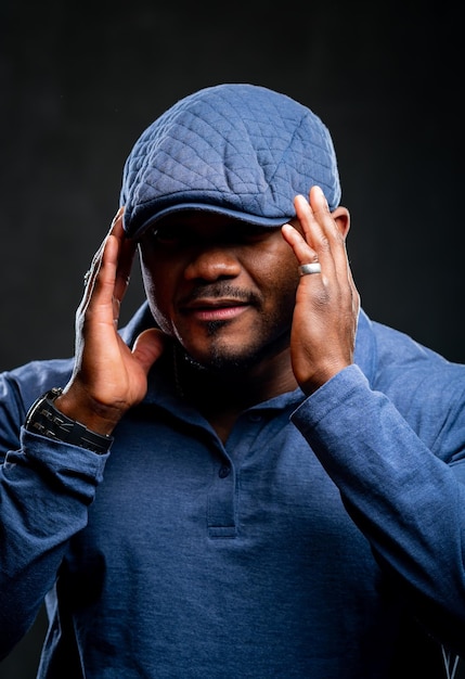 Stylish african american puts on fashion blue cap Dark background Selective focus Closeup