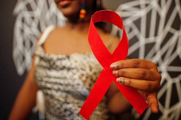 Stylish african american woman hold red ribbon against wall with wings