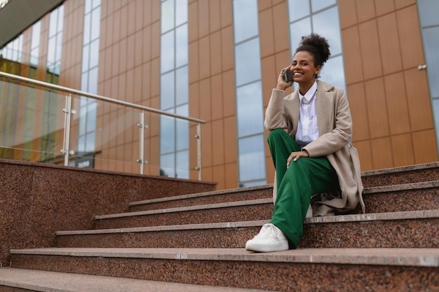 Stylish african american woman quant developer talking on mobile phone while sitting on steps of