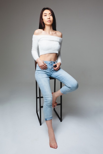 Stylish asian female sitting on chair isolated on gray background