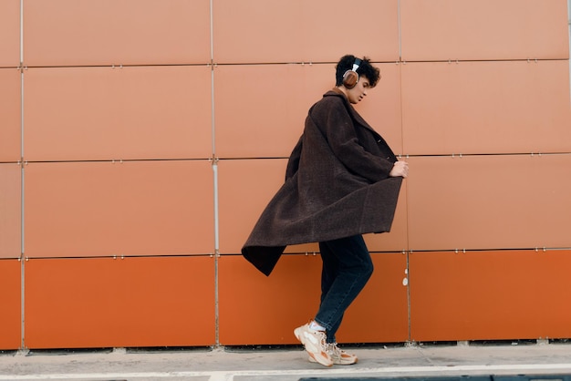 Photo stylish asian woman in brown coat and black pants walking against orange brick wall