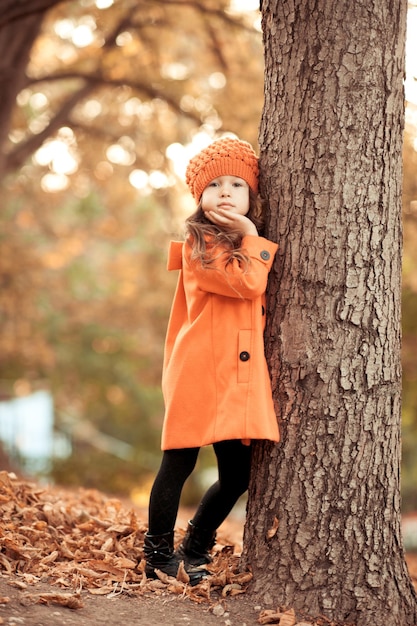 Stylish baby girl wearing trendy autumn jacket and knitted hat outdoors