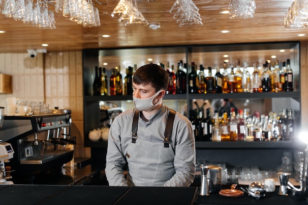 A stylish bartender in a mask and uniform during a pandemic is preparing cocktails at a party The work of restaurants and cafes during the pandemic