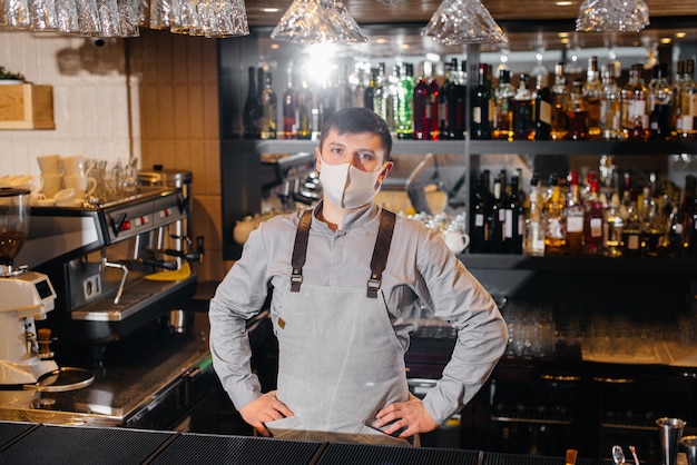 A stylish bartender in a mask and uniform during a pandemic. The work of restaurants and cafes during the pandemic.