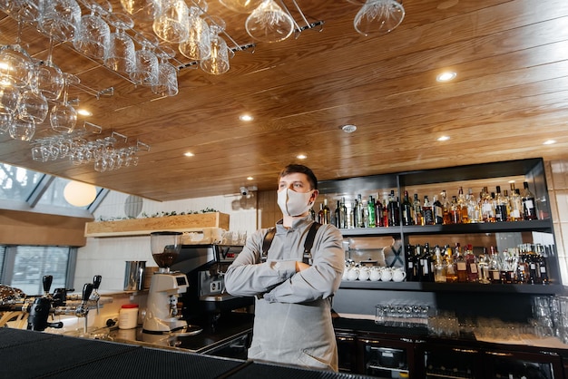 A stylish bartender in a mask and uniform stands near the bar during the pandemic The work of restaurants and cafes during the pandemic