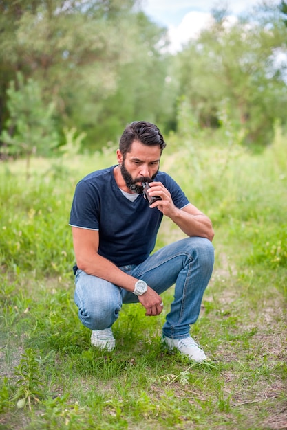 Stylish bearded man is resting in nature and vaping and letting off steam from an electronic cigarette. Non-tobacco smoking.