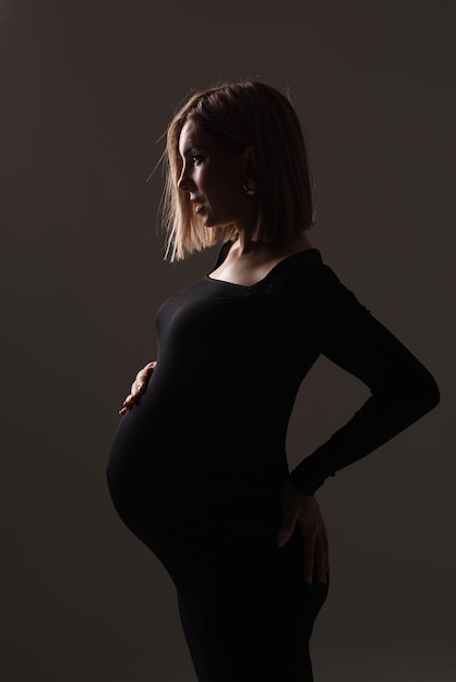 Stylish beautiful pregnant woman in a black dress holds her hands on her stomach