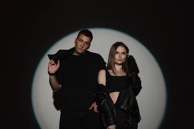 Stylish beautiful young couple in fashionable black casual black clothes on a black background with a circle light in the studio Handsome man and beautiful girl at a party